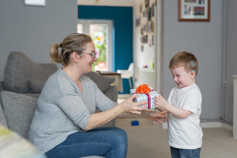 A woman and young child in a front room exchange a gift-wrapped present