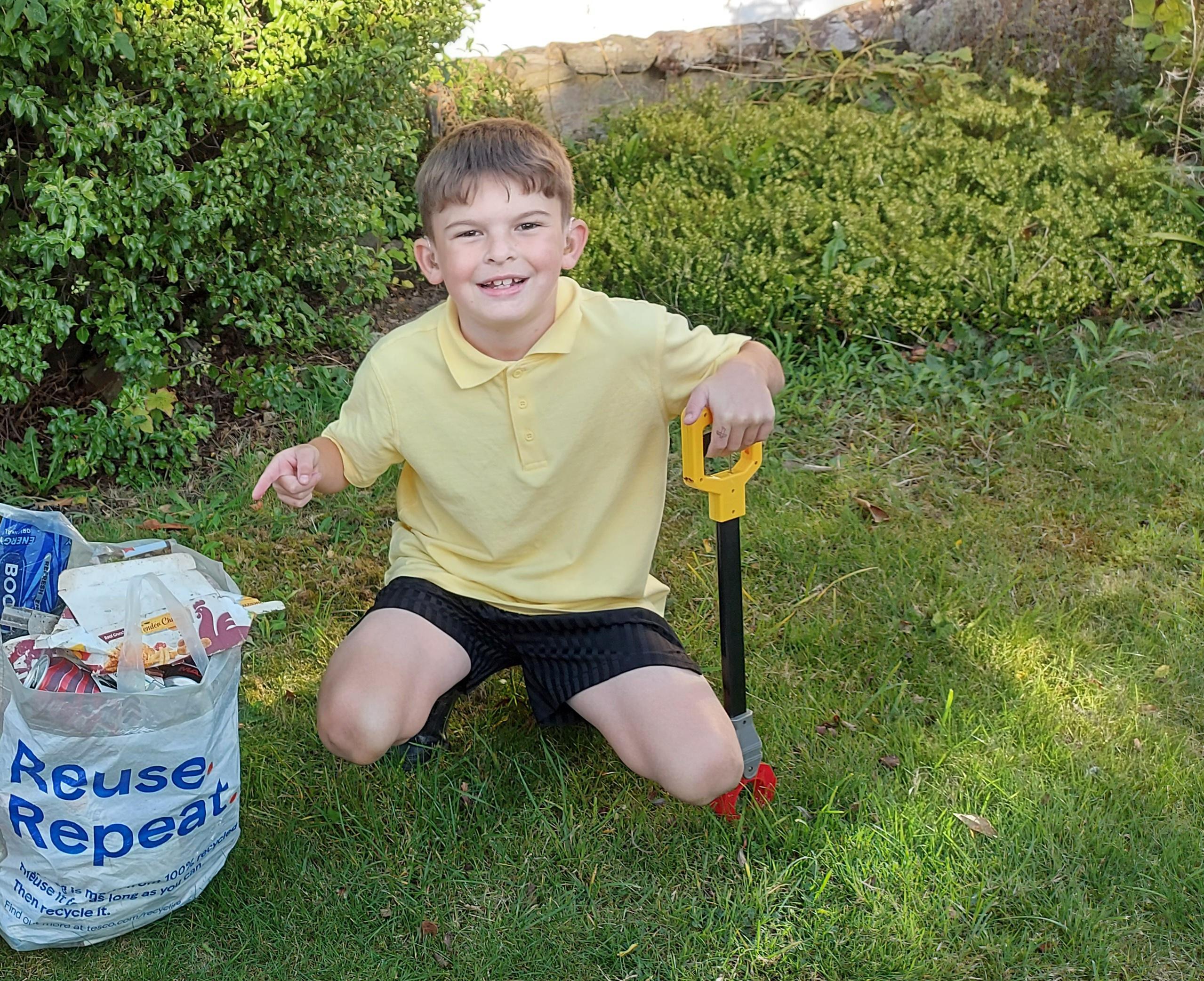 Oliver wearing a yellow polo shirt crouching and pointing to the litter he has picked.
