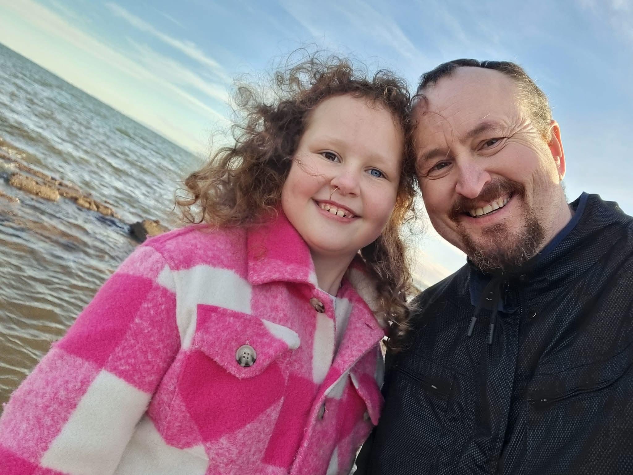 A young girl smiling with her father at the beach