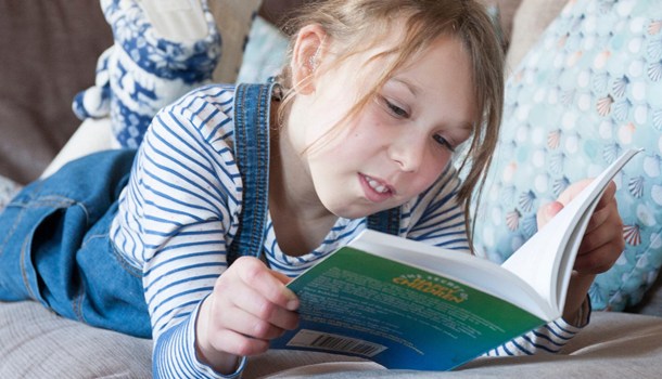 Deaf child lying on the sofa reading a book