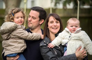 A mom and dad hold their toddler and baby.