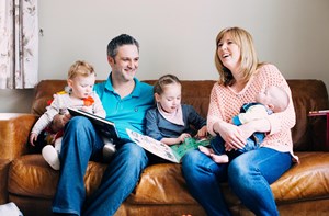 Family sat smiling and reading on a sofa