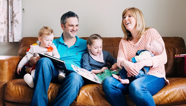 Family sat smiling and reading on a sofa