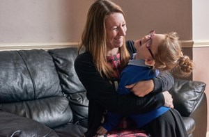 A smiling mum hugs her daughter on the sofa. 