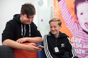 A smiling teenage boy shows his friend something on his phone.