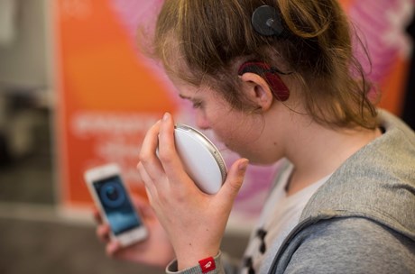 A teenage girl with a hearing implant holding a Smartshaker alarm system and her phone 