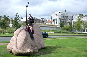 School children sitting on top of a statue in a grassy area