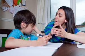 A woman sat next to her son and signing to him while he does school work.