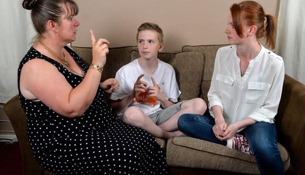A mom signs to her two teenage children sitting on the sofa. 
