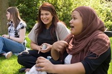 A group of young women talk to each other while sitting on the ground outside. 