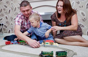 A young deaf boy playing with a train set with his parents.