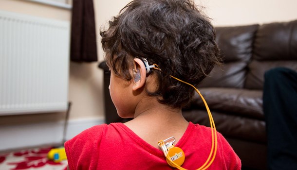 The back of a boy's head who is wearing a hearing aid with a cord and clip that attaches to his shirt.