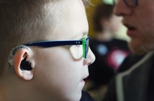 A closeup of a boy with glasses wearing a hearing aid. 