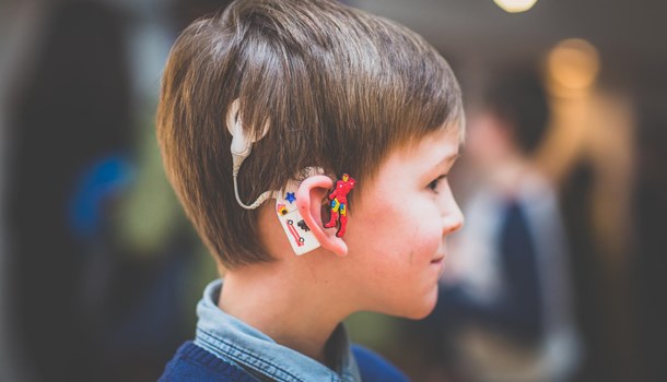 A boy wears a cochlear implant that has been decorated with stickers and a superhero tube attachment. 