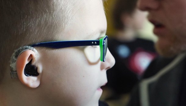 A close-up of a boy wearing a hearing aid and glasses. 