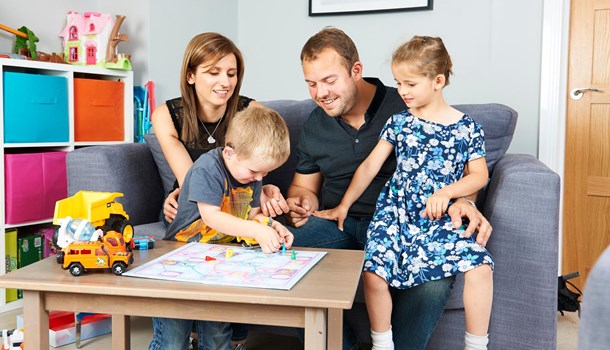 A deaf boy wearing hearing aids playing a board game with his parents and sister.