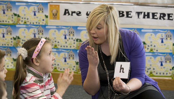 A primary teacher shows a pupil how to pronounce the 'h' sound.