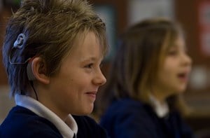 A boy in school uniform wearing a cochlear implant smiles.
