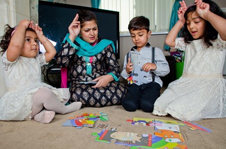 A mom and her three young children play a game in their living room while signing to each other