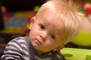 A toddler wearing a hearing aid looks quizzically at the camera