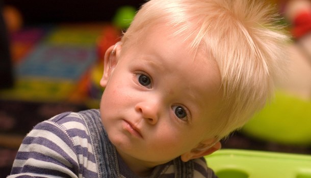 A toddler wearing a hearing aid looks quizzically at the camera