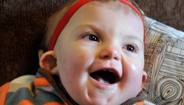 A baby wearing a headband smiles happily.