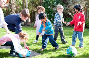 A group of young children play with a bubble machine in a back garden.