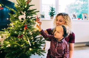 A mum helps her son to hang a bauble on a Christmas tree.