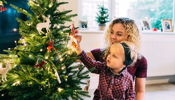 A mum helps her son to hang a bauble on a Christmas tree.