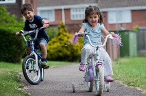 Two children bike on a paved path.