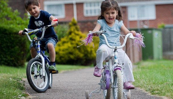 Two children bike on a paved path.
