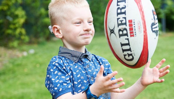A boy wearing a bone conduction hearing implant tosses a rugby ball. 