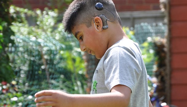 A boy wearing a cochlear implant stands in his back garden.