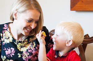 A mom smiles at her son who holds up a small yellow plastic item. 