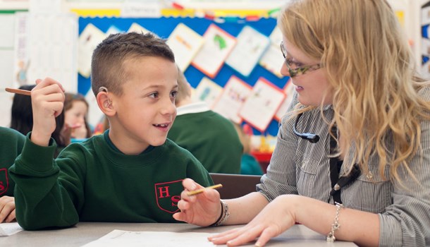 A teacher with a listening loop works one-on-one with a pupil wearing hearing aids.