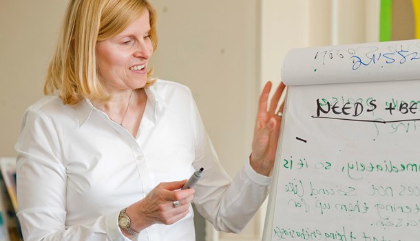 A woman holds a marker while standing by a flipchart.