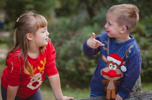 A boy and girl in Christmas jumpers sign to each other.