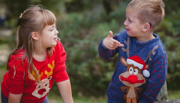 A boy and girl in Christmas jumpers sign to each other.