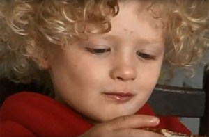 A young boy with curly blond hair looks at an object he is holding.