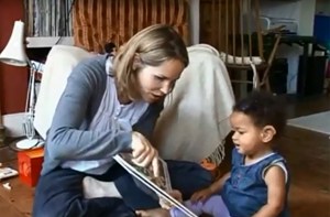 A mum points at a picture book with her baby who is wearing hearing aids.