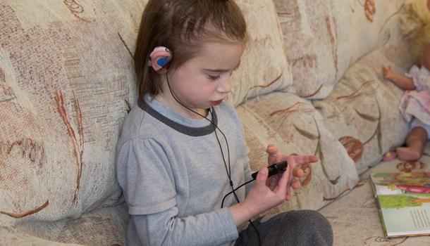 Young girl with hearing aids sitting on a sofa