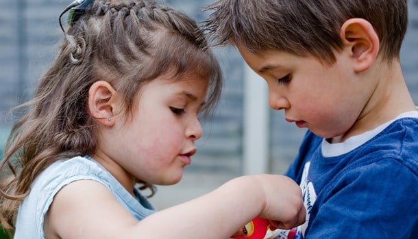 A young girl wearing a hearing implant shares a toy with a boy.
