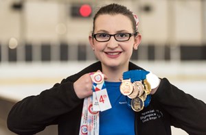 A girl holds up multiple award ribbons and medals. 