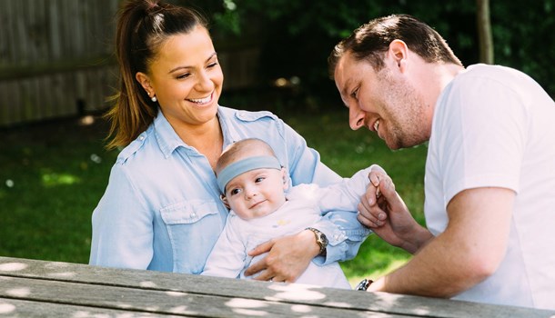Eight month old Frederick being held by his parents at a picnic bench.