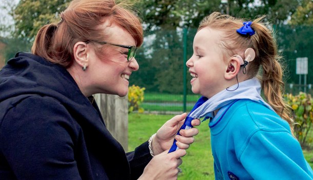 Adalaide's mum tying the scarf of her Beavers group outfit that matches her blue cochlear implant.