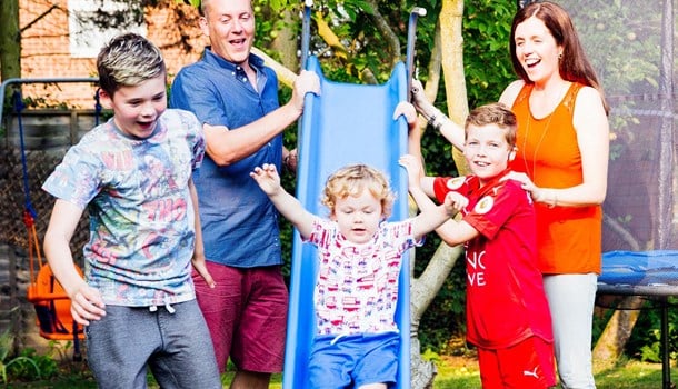 Alfie sliding down a slide with his parents and brothers standing next to him.