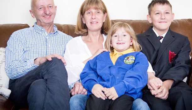 Megan, her parents and brother sat on the sofa smiling at the camera.