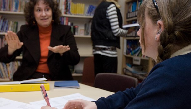 A teacher signs to a girl wearing a hearing aid.