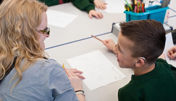 A teacher works one-on-one with a pupil wearing a hearing aid.