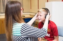An audiologist adjusts headphones over a boys ears.